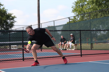 A senior athlete hits a shot, competing in singles, of a pickleball tournament.