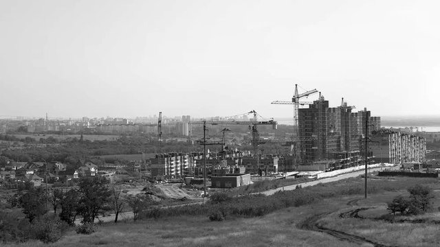 Several tower cranes build a multi-storey building and move cargo, long-range plan, time-lapse, monochrome
