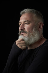 Portrait of a brutal gray haired man with a gray lush beard and strict face on a black background, selective focus