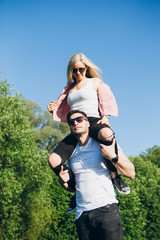 Girl sitting on the back of a man hugging and smiling in nature in summer