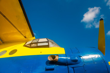 Detail of an old  airplane in blue and yellow colors in front of a clear sky