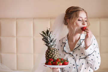 Young woman having breakfast in bed and eating strawberries