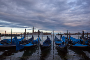 Fototapeta na wymiar Gondolas in Venice at dusk taken on the shoreline besides the Piazza San Marco / St Marks Square.The image was taken during a dramatic sunset.