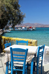 Typical blue chairs and table of Greece overlooking fishing harbour and turquoise Aegean Sea, Naxos, Greek Islands