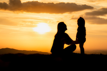 Fototapeta na wymiar silhouette of woman on top of mountain with your daughter in sunset