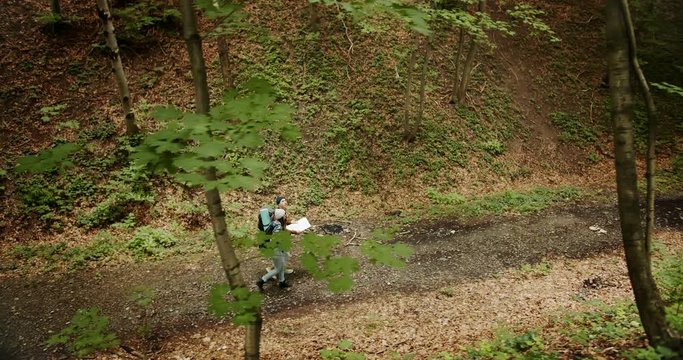 Couple of backpacked hikers walking on forest road and checking direction on paper map, trakking