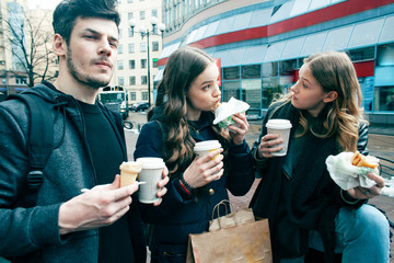 lifestyle and people concept: two girls and guy eating fast food on city street together having fun, drinking coffee