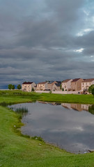 Fototapeta premium Vertical Scenic neighborhood park with a shiny pond and pathway under an overcast sky