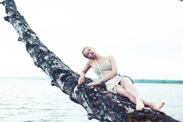 young blond woman hanging on birch tree at lake shore, summer vacations outdoor lifestyle