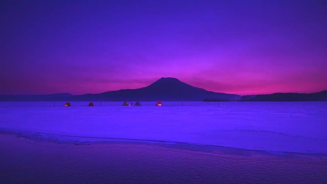 Mount Akan and tents pitched in snow at purple dawn