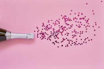 Champagne bottle with pink confetti stars on light pink background. Flat lay of christmas, anniversary, bachelorette, new year celebration concept. Copy space, top view