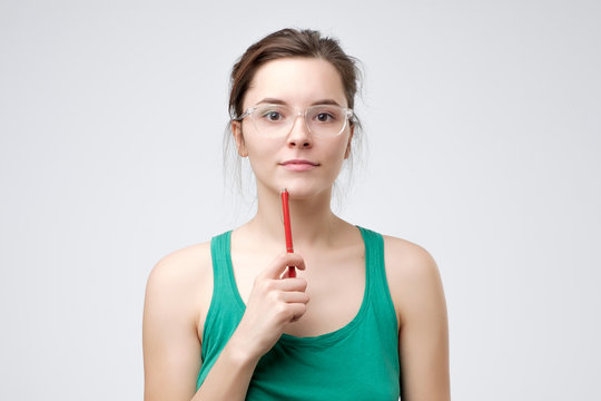 Young caucasian woman with glasses and pen looking at camera with slight smile. She is getting prepared to exam. Studio shot