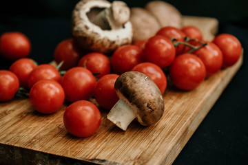 Champignons mushrooms and cherry tomatoes on wooden board on black background