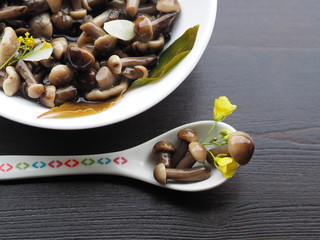 Delicious, beautiful, small pickled mushrooms in a dessert spoon close-up. Home recipe - delicious pickles with garlic, pepper, Bay leaf, cherry leaf and herbs in a white plate on a wooden table.