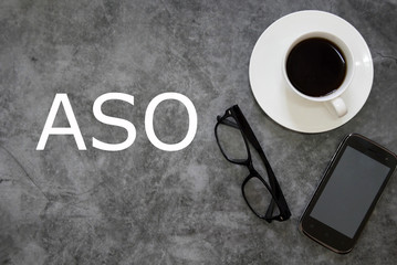 Top view of a cup of coffee, sunglasses and mobile phone on grey floor background written with ASO.