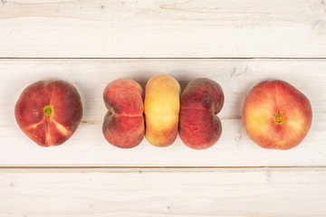 Group of five whole fresh red peach prunus persica platycarpa arranged symmetrically flatlay on white wood