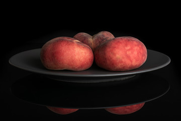 Group of three whole fresh red peach prunus persica platycarpa on gray ceramic plate isolated on black glass