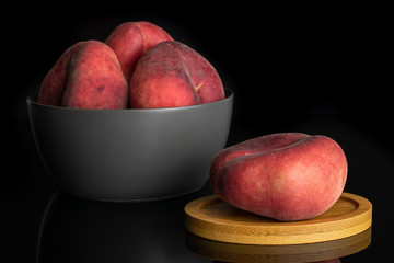 Group of four whole fresh red peach prunus persica platycarpa in gray ceramic bowl on round bamboo...