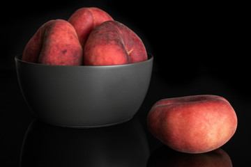 Group of four whole fresh red peach prunus persica platycarpa in gray ceramic bowl isolated on black glass
