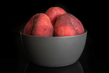 Group of three whole fresh red peach prunus persica platycarpa in gray ceramic bowl isolated on black glass