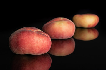 Group of three whole fresh red peach prunus persica platycarpa placed diagonally in line isolated on black glass