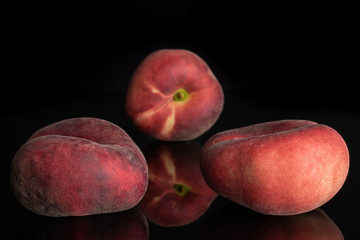 Group of three whole fresh red peach prunus persica platycarpa isolated on black glass