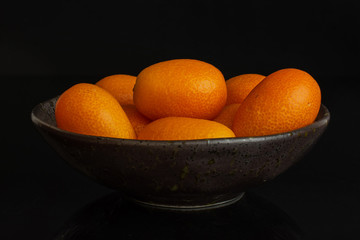 Lot of whole fresh orange kumquat in a dark ceramic bowl isolated on black glass
