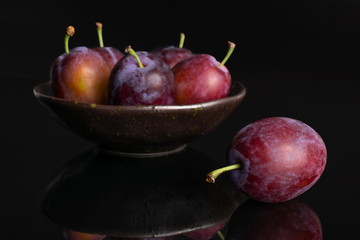 Group of six whole fresh blue plum in a dark ceramic bowl isolated on black glass