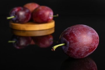Group of four whole fresh blue plum on a round bamboo coaster isolated on black glass
