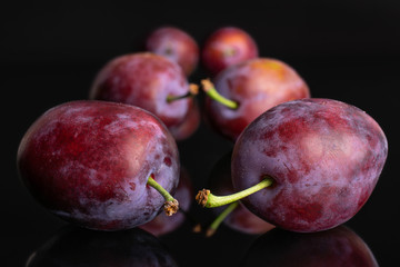 Group of six whole fresh blue plum arranged symmetrically isolated on black glass