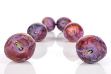 Group of six whole fresh blue plum arranged symmetrically isolated on white background