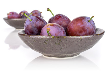 Lot of whole fresh blue plum in a dark ceramic bowl isolated on white background