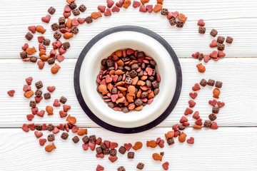 Dry dog food in bowl on white wooden background top view