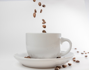 Coffee beans fall into a white porcelain cup and saucer, bouncing and jumping through the air conveying alert excitement, all isolated against a white background