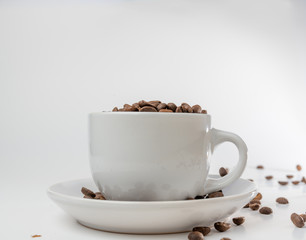 Coffee beans fall into a white porcelain cup and saucer, bouncing and jumping through the air conveying alert excitement, all isolated against a white background
