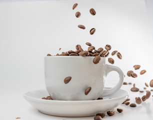 Coffee beans fall into a white porcelain cup and saucer, bouncing and jumping through the air conveying alert excitement, all isolated against a white background