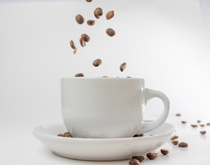 Coffee beans fall into a white porcelain cup and saucer, bouncing and jumping through the air conveying alert excitement, all isolated against a white background