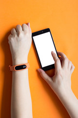 Fitness tracker on a woman hand on an orange background and mock up of smartphone.