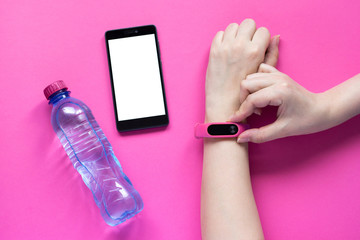 Fitness tracker on a womans hand, smartphone and a bottle of water on pink background. - 281709595