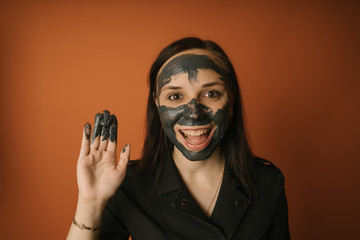 A young woman inflicts a black mask on the face on an orange background. The concept of healthy lifestyle, beauty, body care.