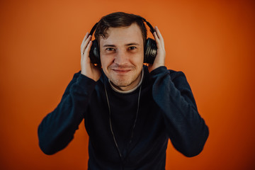 A beautiful young man in headphones with ears is dancing on an orange background. The concept of International Music Day.