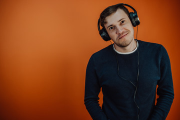 Fototapeta premium A beautiful young man in headphones with ears is dancing on an orange background. The concept of International Music Day.