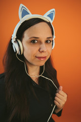 A beautiful young woman in headphones with ears is dancing on an orange background. The concept of International Music Day.