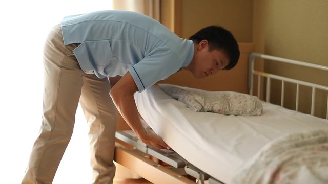 Male healthcare professional making bed at nursing house, Japan