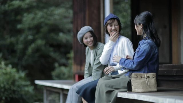 Three female tourists sitting at temple and talking, Kyoto, Japan