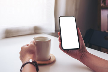 Mockup image of a woman holding black mobile phone with blank desktop screen while drinking coffee