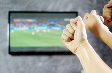 Hand of young man raised his fist for cheer up football player in front of TV at home. Cheer football Concept.