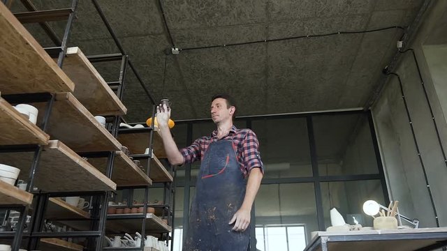 Male potter looking to the handmade vases during work day in the pottery.