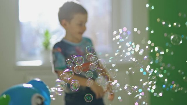 Many aqua bubbles flying in the room on blurred background with a little boy. Cute child having fun with soap bubbles indoors.