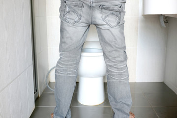 Rear view Leg of man standing peeing to toilet bowl in restroom at home. Health concept